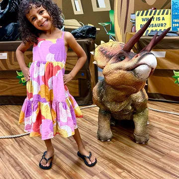 A girl stands beside the walking triceratops